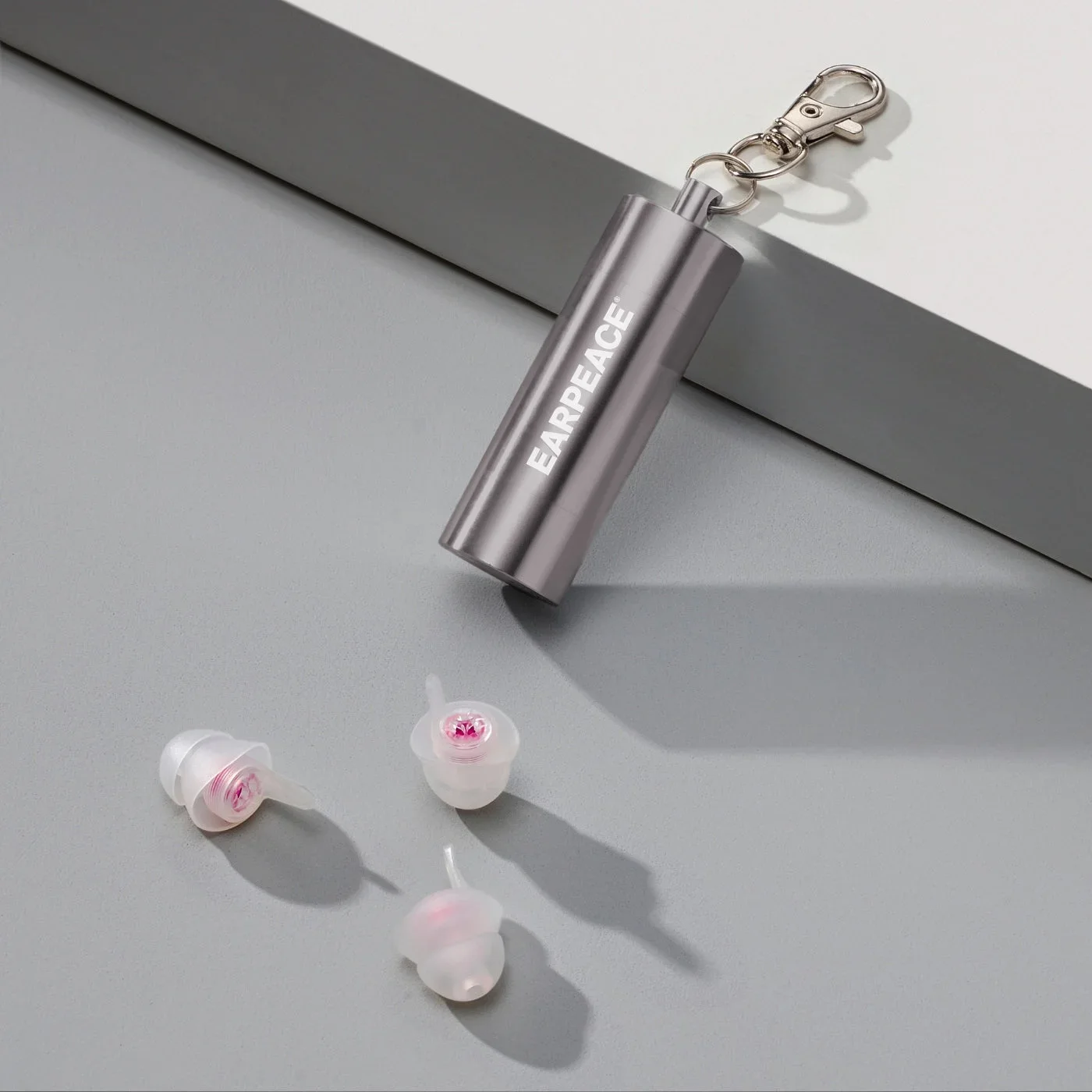 Three clear EARPEACE MUSIC PRO earplugs with pink filters beside the metal carry case.