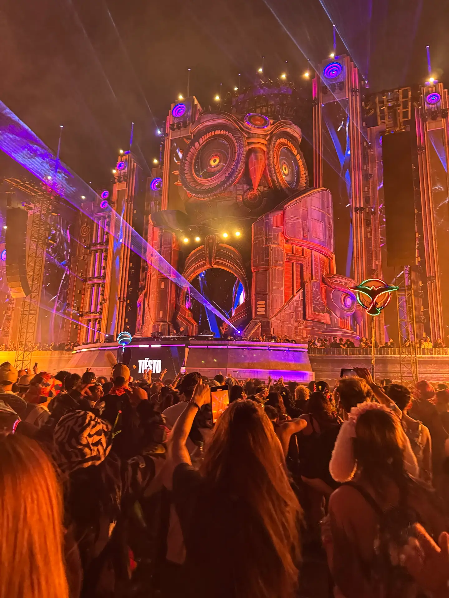 Owl-shaped festival stage glowing orange and violet above a nighttime crowd